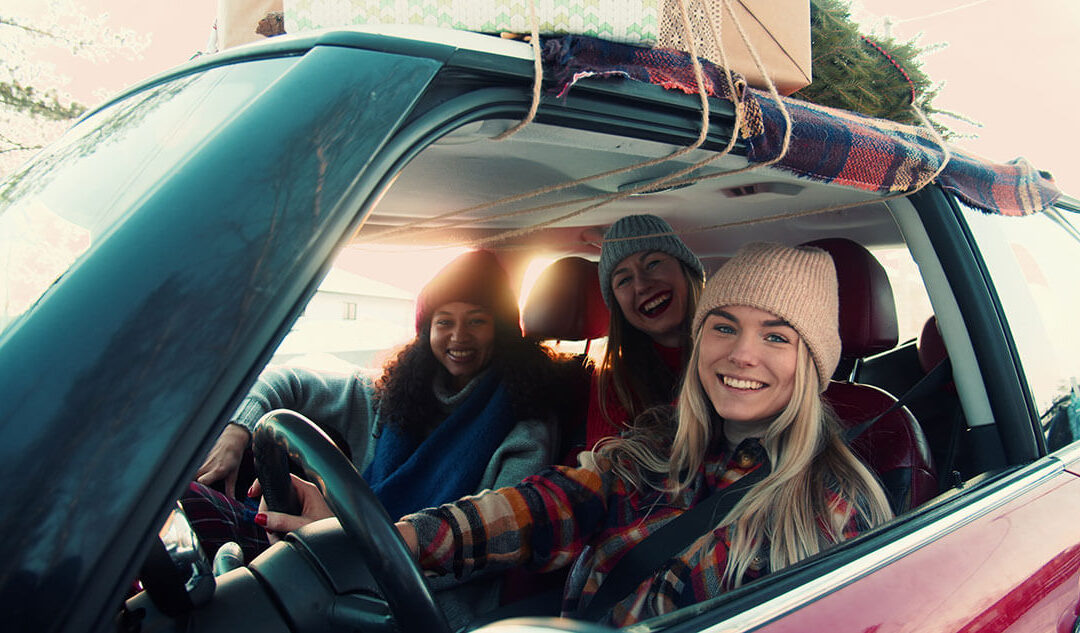 Three happy young women in fancy red car on snowy winter road